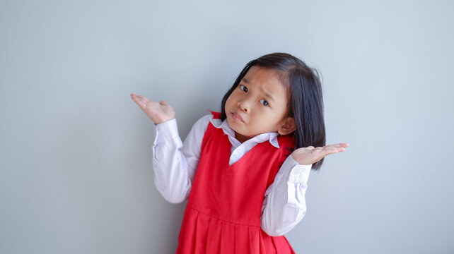 Asian child wearing school uniform with mouth full of food. i don't know gesture.