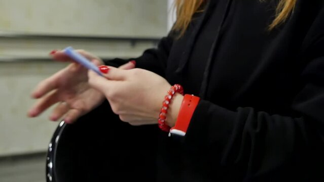 Trainer woman hands with red manicure holding a fountain pen gesturing explains to a group of athletes how to do exercises. On the woman's hand is a red smart watch and a red scrunchy