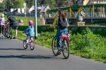 Fototapeta premium Authentic group of people riding bikes down the street on a sunny day, trending photo, mother and child, father and child, wide green lanes, long shade, sustainable eco-friendly transportation