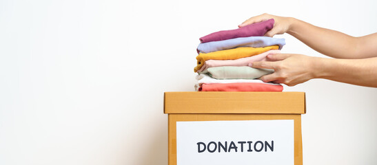 Donation, Charity, Volunteer, Giving and Delivery Concept. Hand holding Clothes into Donation box at home or office for support and help poor, refugee and homeless people. Copy space for text