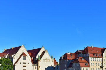 Fototapeta na wymiar Old buildings with beige walls and red roofs on the horizon, and a wide background of blue cloudless sky. Ancient architecture. Cityscape view. Sunny summer day. Poland, Poznan, July 2022.