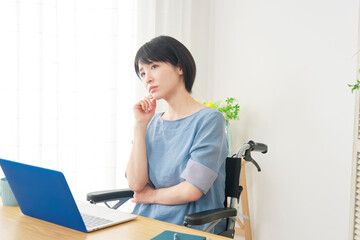リビングでノートパソコンの前で考える車椅子に乗った女性
