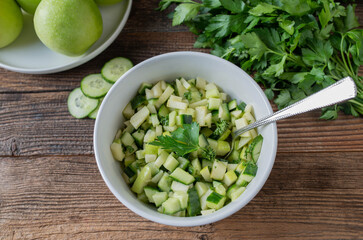Fruit vegetable salad with marinated green apples and cucumber in a bowl on wooden table