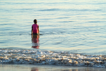 Little asian girl in pink standing turn back in the sea with wave sea foreground