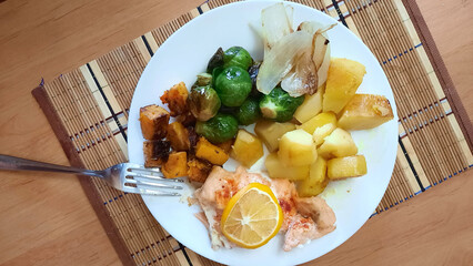Healthy lunch: stewed potatoes, pumpkin, fried onions, Brussels sprouts. Also on the plate is fried red fish with lemon.