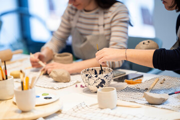 Crop women decorating clay cups with brush