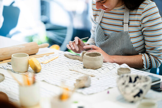 Crop woman making ornament on clay in workshop