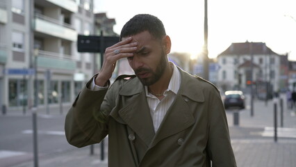 Frustrated young man walking in city street feeling disbelief. One Male Middle Eastern person walks in sidewalk suffering from regret and anxiety