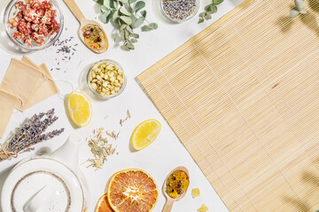 Healing tea from wild plants and flowers. Home herbal apothecary concept. Sustainable flat lay with dry flowers and herbs, tea bags, lemons and spoons with empty wooden napkin on white background