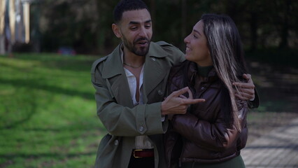 A joyful young Arab couple walking outside at park during sunny day. Happy man and woman in conversation