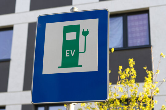 EV - electric vehicle charging station sign on a pillar with building and yellow flowers background.