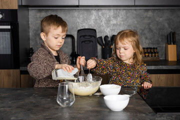 Little siblings cooking together on a modern kitchen, helping each other and having fun while...