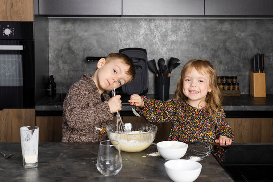 Little Siblings Cooking Together On A Modern Kitchen, Helping Each Other And Having Fun While Mother Is Gone.