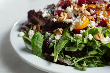 A closeup view of a garden salad, featuring crumble cheese, walnut, beets, and mandarin wedges.
