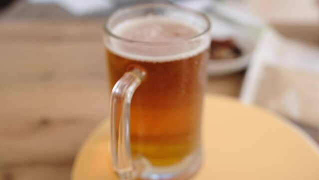 Close-up glass of cold beer on the table. Glass full light craft beer spin with drop of condensation cold drink. Cold alcohol beer drink in mug. Drink glass on table. 