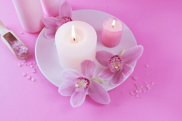 Fresh pink orchid flowers, burning candles, sea salt, on a bright pink background