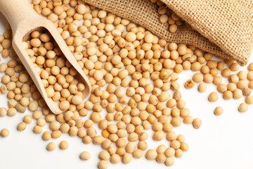Granos de soja junto a una bolsa de arpillera y una cuchara pala de madera sobre un fondo blanco. Vista de superior y de cerca. Copy space