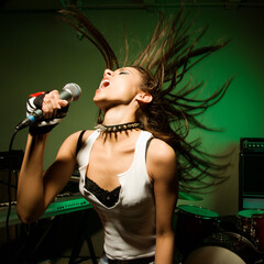 Caucasian female swinging head and hear while singing into microphone.