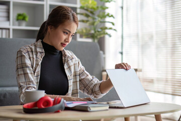 Attractive Asian female freelancer planning her project, working on her tasks on laptop computer at a coffee table in her living room.