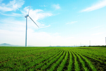 Wind turbine standing against a blue skywith some clouds in a green grass field