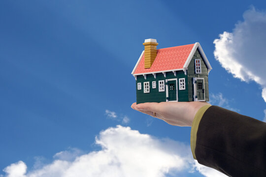 Miniature house in woman hand held against blue skies - real estate concept