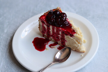 Slice of cheesecake with berry sauce on white plate. Homemade cheesecake with blackcurrant jam on top. Sweet food close up photo. Space for text. 