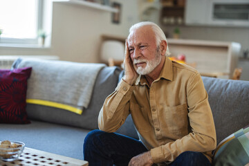 Close-up of senior man having headache. Cropped shot of stressed senior man sitting in the living room.