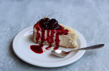 Slice of cheesecake with berry sauce on white plate. Homemade cheesecake with blackcurrant jam on top. Sweet food close up photo. Space for text. 