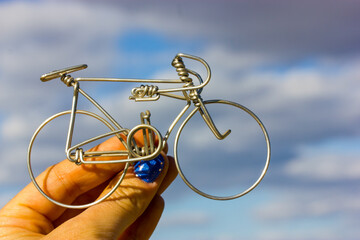 A metal bicycle in a woman's hand against a blue-gray cloudy sky. Holding a toy mini bike. Cycling in mountains. Round aluminum wheels of a bike. Healthy lifestyle, outdoor leisure and sports concept.