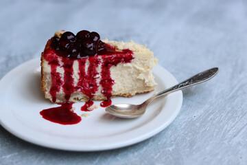 Slice of cheesecake with berry sauce on white plate. Homemade cheesecake with blackcurrant jam on top. Sweet food close up photo. Space for text. 