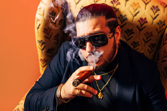 Calm man smoking cigar in armchair in studio