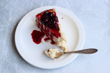 Slice of cheesecake with berry sauce on white plate. Homemade cheesecake with blackcurrant jam on top. Sweet food close up photo. Space for text. 