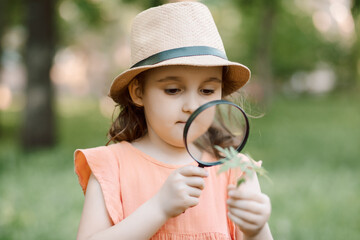 Caucasian little cute girl exploring nature environment with a magnifying glass loupe