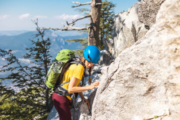 The girl is climbing the rock. Woman climber with a backpack and a helmet in the mountains....
