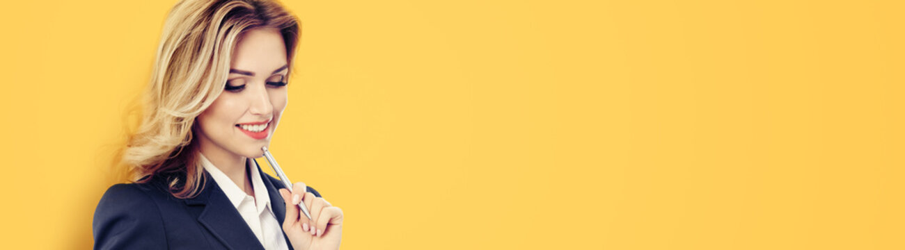 Wide banner image - thinking young businesswoman in dark suit writing, isolated over orange yellow color background. Business success concept. Copy space empty area for some text or slogan.