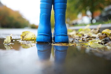 legs of child in blue rubber boots jumping in the autumn puddles