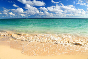 Fototapeta na wymiar Tropical sandy beach with advancing wave and blue sky
