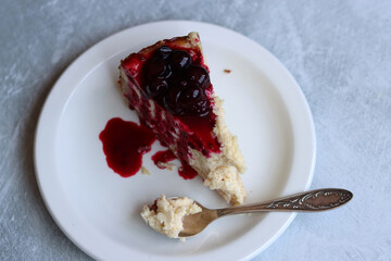 Slice of cheesecake with berry sauce on white plate. Homemade cheesecake with blackcurrant jam on top. Sweet food close up photo. Space for text. 
