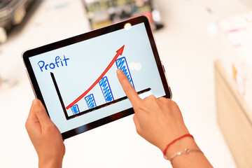 Using tablet to see business growth predication graph with blur background of department store. Business successful concept. Concept of growth planning and strategy.