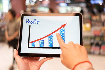 Using tablet to see business growth predication graph with blur background of department store. Business successful concept. Concept of growth planning and strategy.