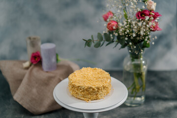 Freshly made delicious puff pastry napoleon cake on a white stand on a background of flowers...
