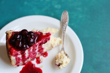 Slice of cheesecake with berry sauce on white plate. Homemade cheesecake with blackcurrant jam on top. Sweet food close up photo. Space for text. 