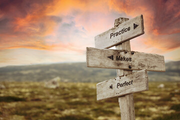 practice makes perfect text quote on wooden signpost outdoors in nature. Pink dramatic skies in the...