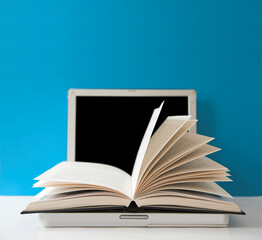 Open book on top of a laptop computer - focus on the tips of the page leaves.