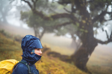 Side view of a backpacker woman in rainproof clothing looking in the distance. Fanal Forest,...