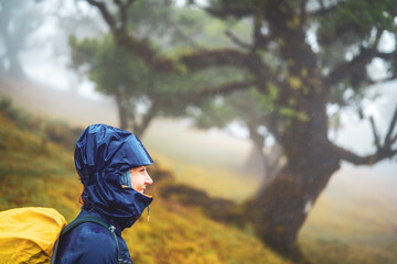 Side view of a backpacker woman in rainproof clothing looking sceptical in the distance. Fanal...