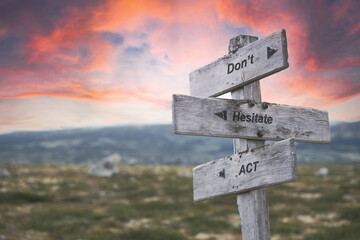 dont hesitate act text quote on wooden signpost outdoors in nature. Pink dramatic skies in the background.