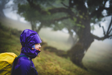 Side view of smiling backpacker woman in rainproof clothes looking into the distance. Fanal Forest, Madeira Island, Portugal, Europe.