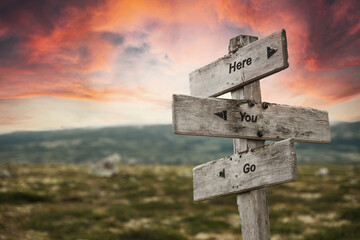 here you go text quote on wooden signpost outdoors in nature. Pink dramatic skies in the background.