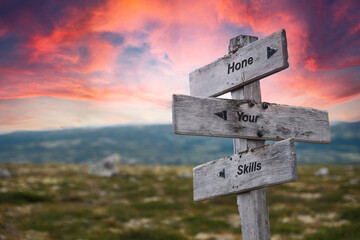 hone your skills text quote on wooden signpost outdoors in nature. Pink dramatic skies in the background.